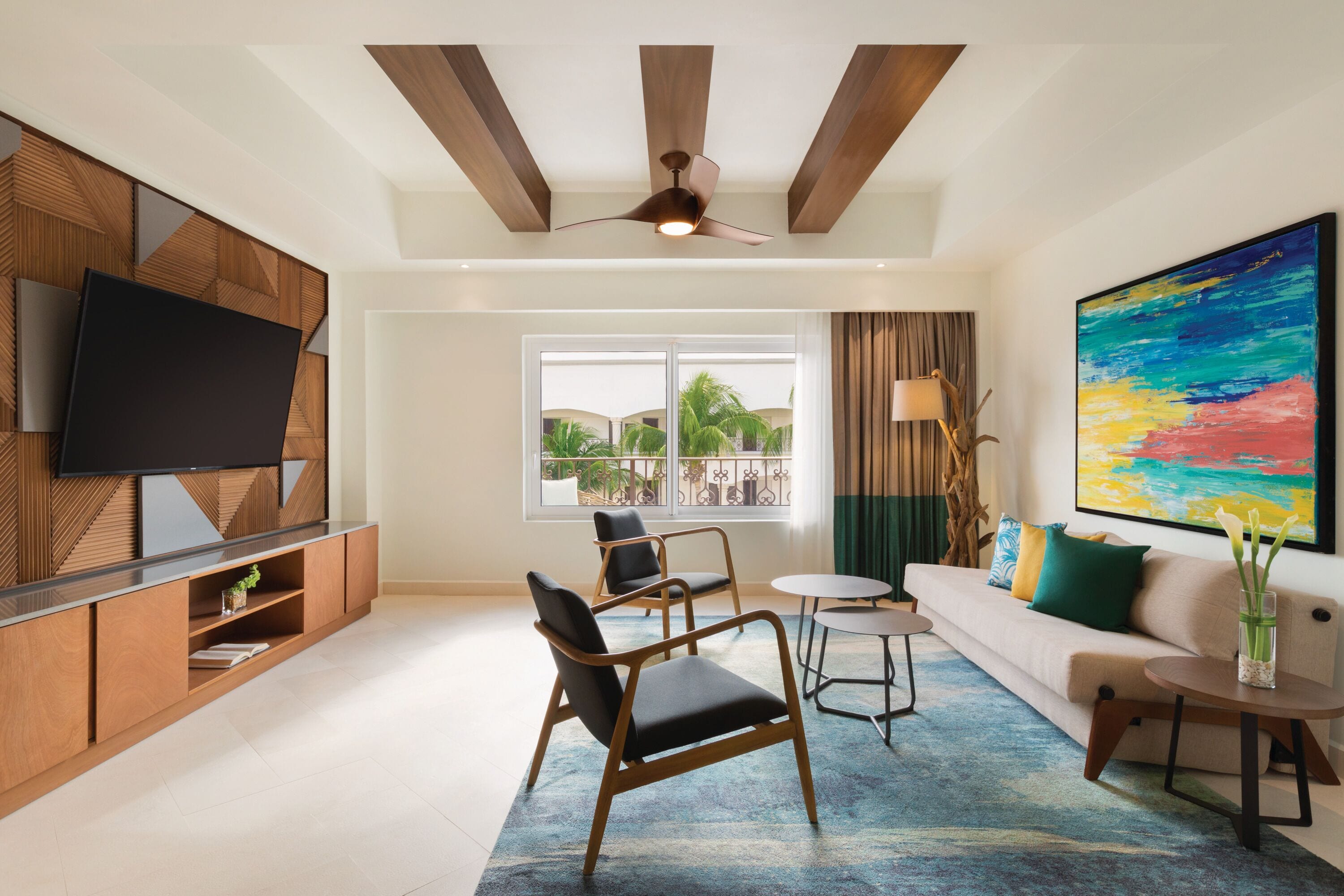 A modern living room with a large TV, a sofa, two armchairs, a coffee table, and a ceiling fan.