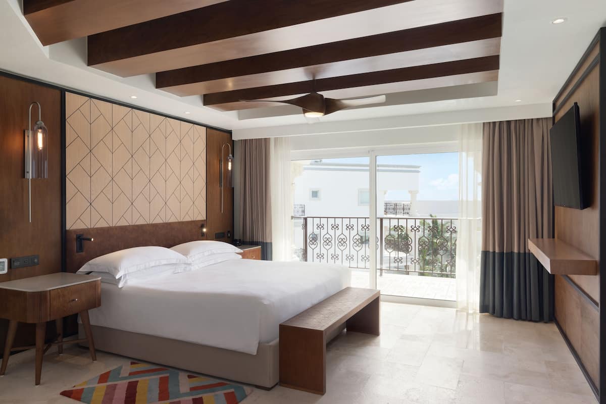Una habitación de hotel moderna con una cama grande, un escritorio, una banca y un balcón con vistas.