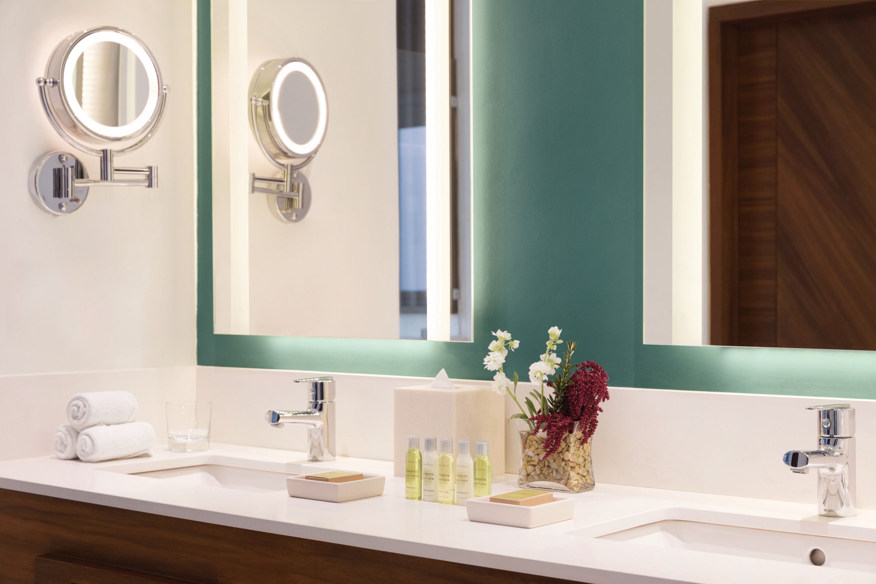 Un baño moderno con dos lavamanos, un espejo grande y un florero con flores.