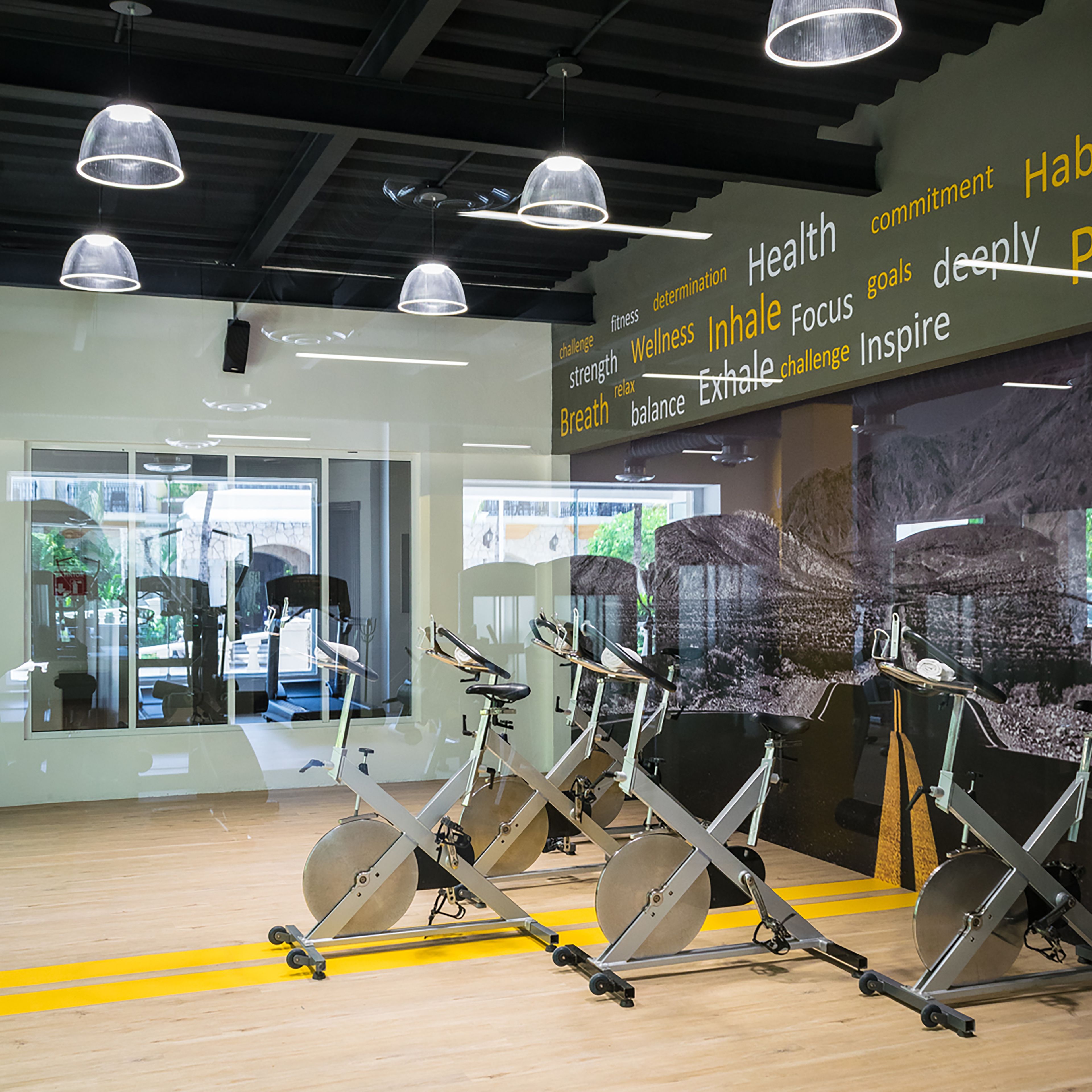 A gym with stationary bikes, a wall with motivational words, and a glass door leading outside.