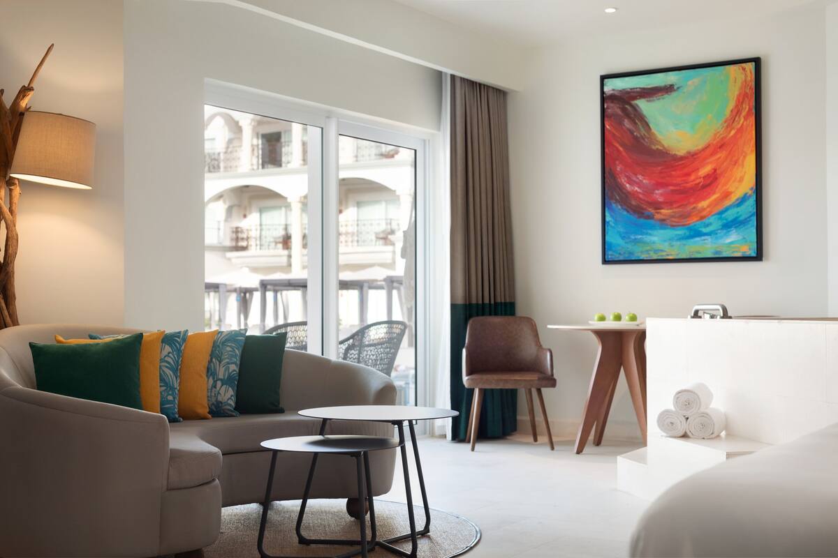Habitación de hotel moderna con sofá, una pequeña mesa redonda, una silla, un cuadro y vistas al balcón.