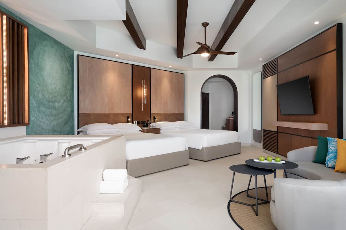 Una habitación de hotel moderna con una cama grande, un baño independiente, un televisor montado en la pared y un ventilador de techo.