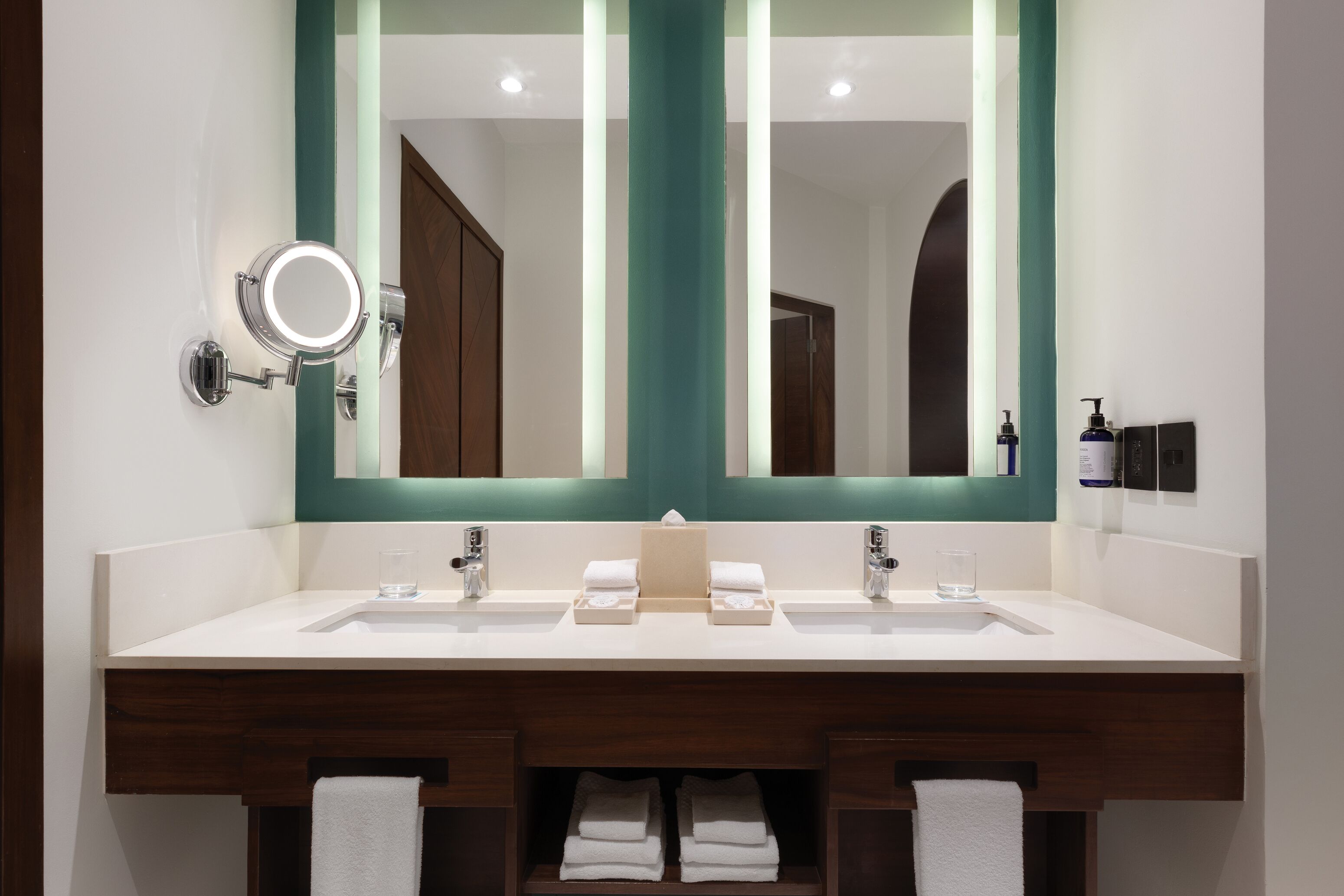 Un baño moderno con un espejo grande, dos lavamanos y un perchero para toallas.