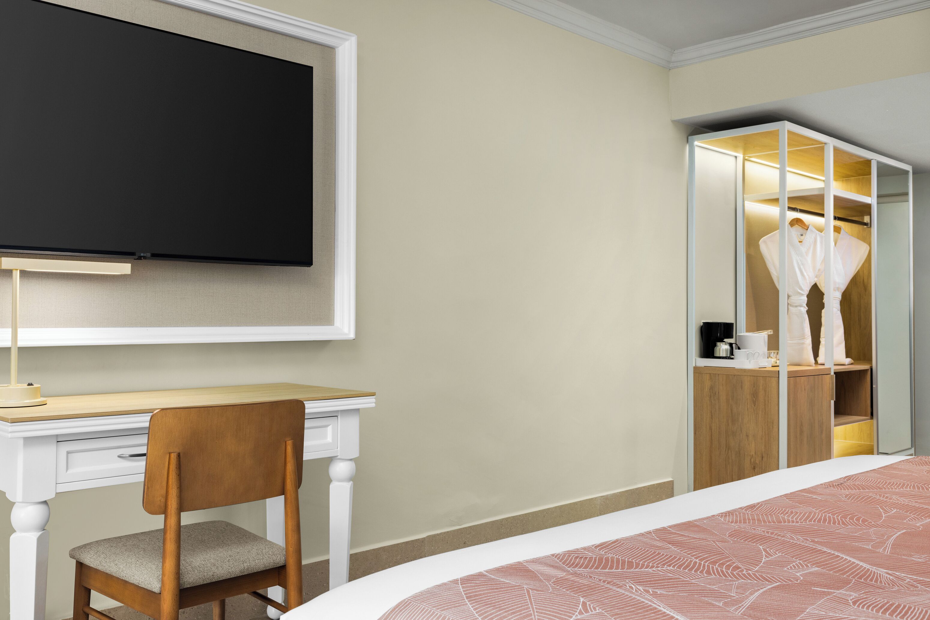 A hotel room with a bed, a desk with a chair, a television mounted on the wall, and a walk-in closet with a mirror.