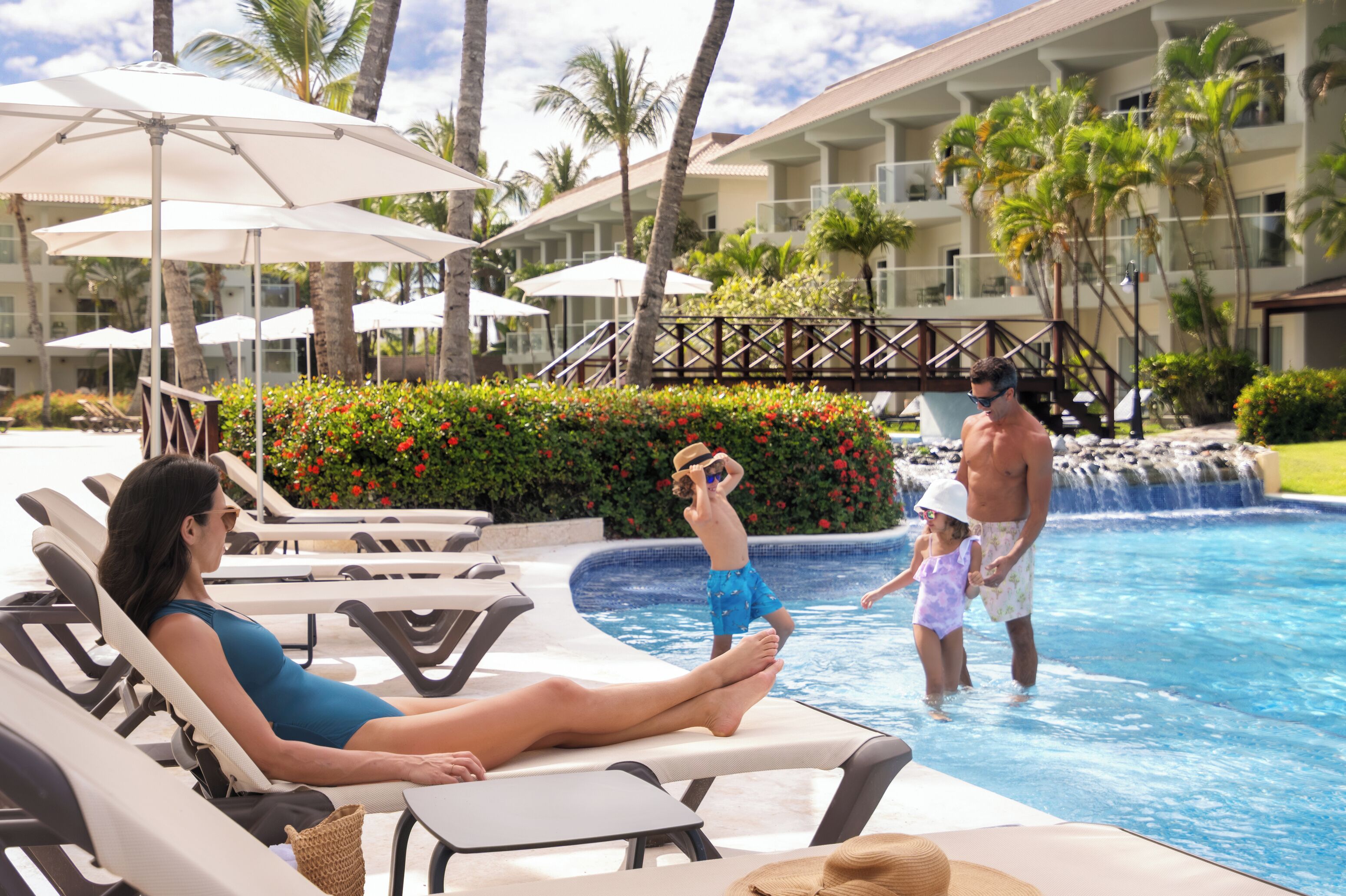 Un espace piscine aménagé avec des chaises longues, des parasols et une cascade décorative.