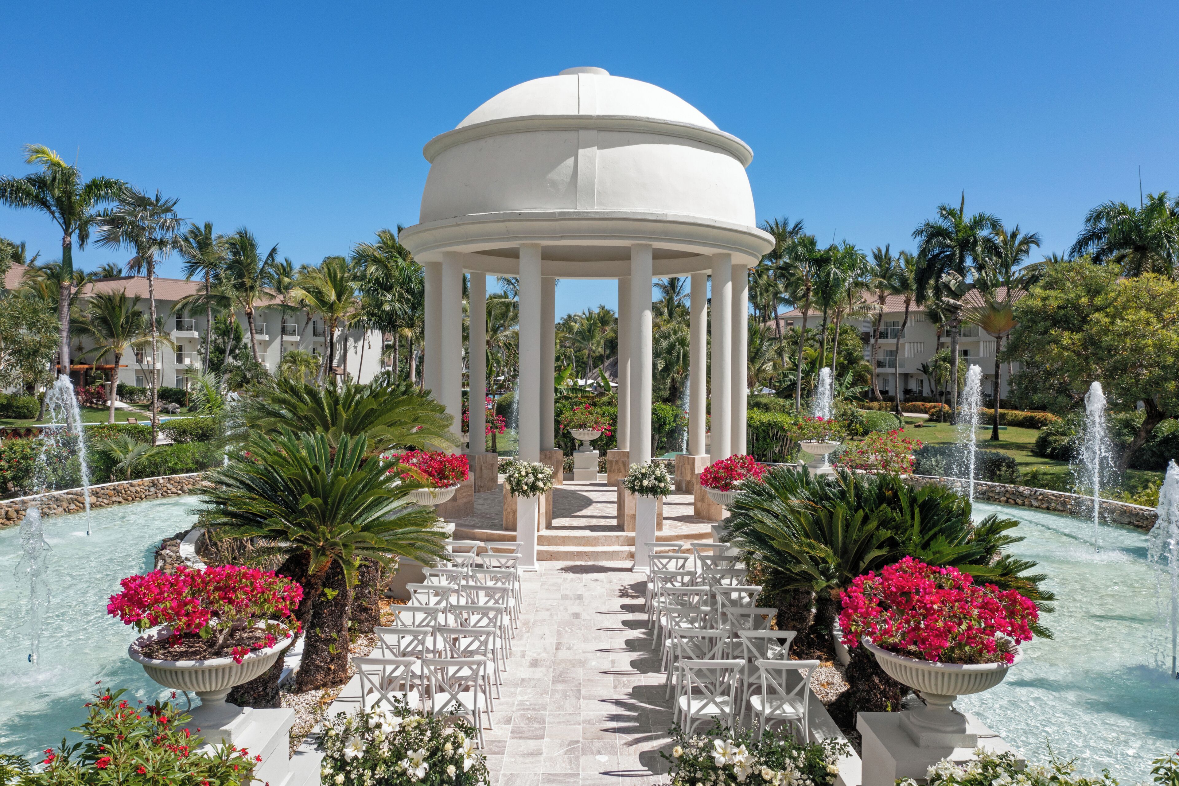 A gazebo with a dome roof, surrounded by a garden with fountains and palm trees.
