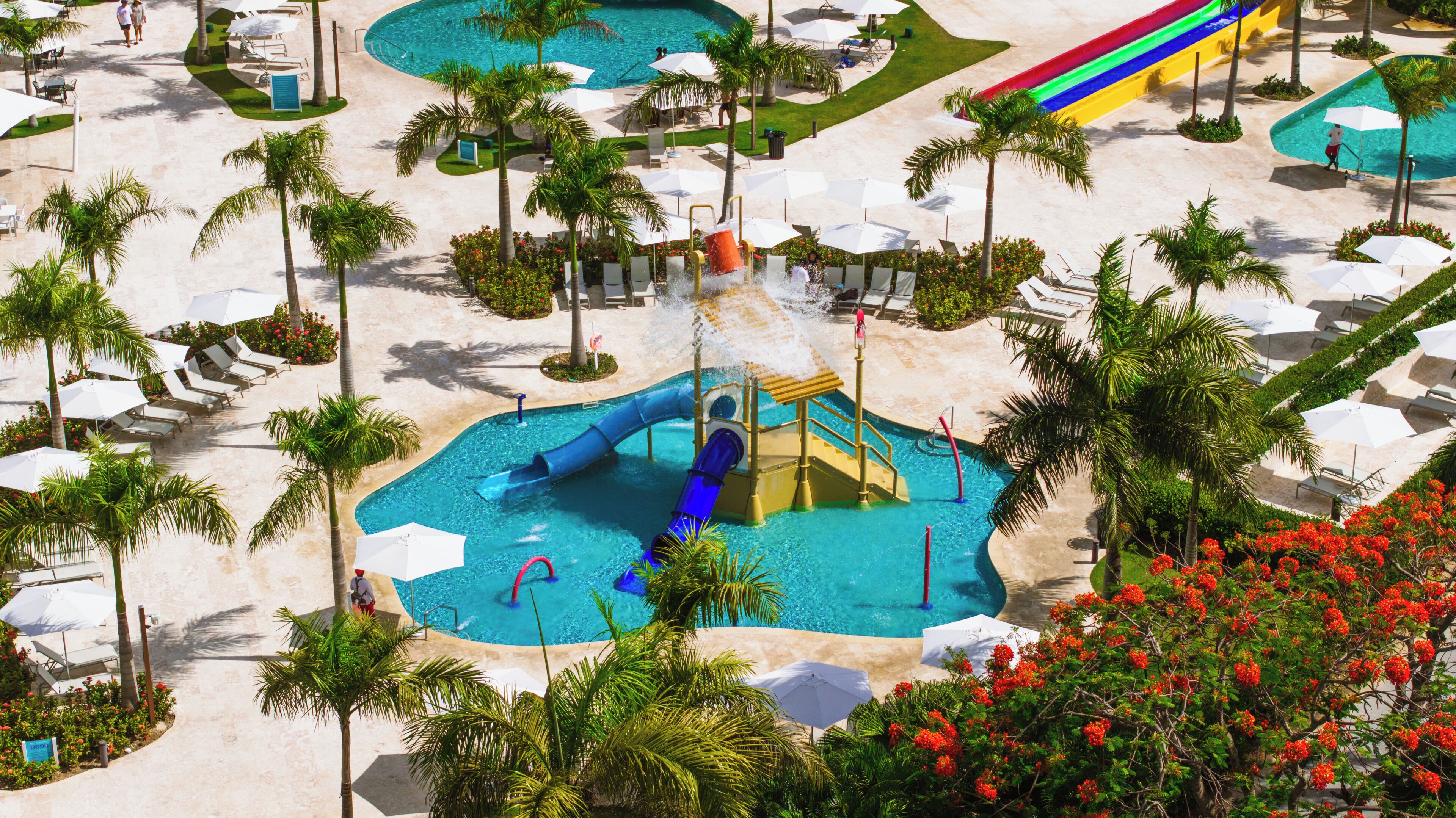 Un complexe hôtelier doté d’un parc aquatique comprenant des toboggans et une zone de piscine, le tout entouré de palmiers et de chaises longues.