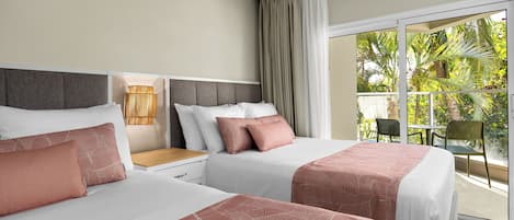 Une chambre d’hôtel avec deux lits, une table de chevet, une lampe et une vue sur un balcon agrémenté de plantes.