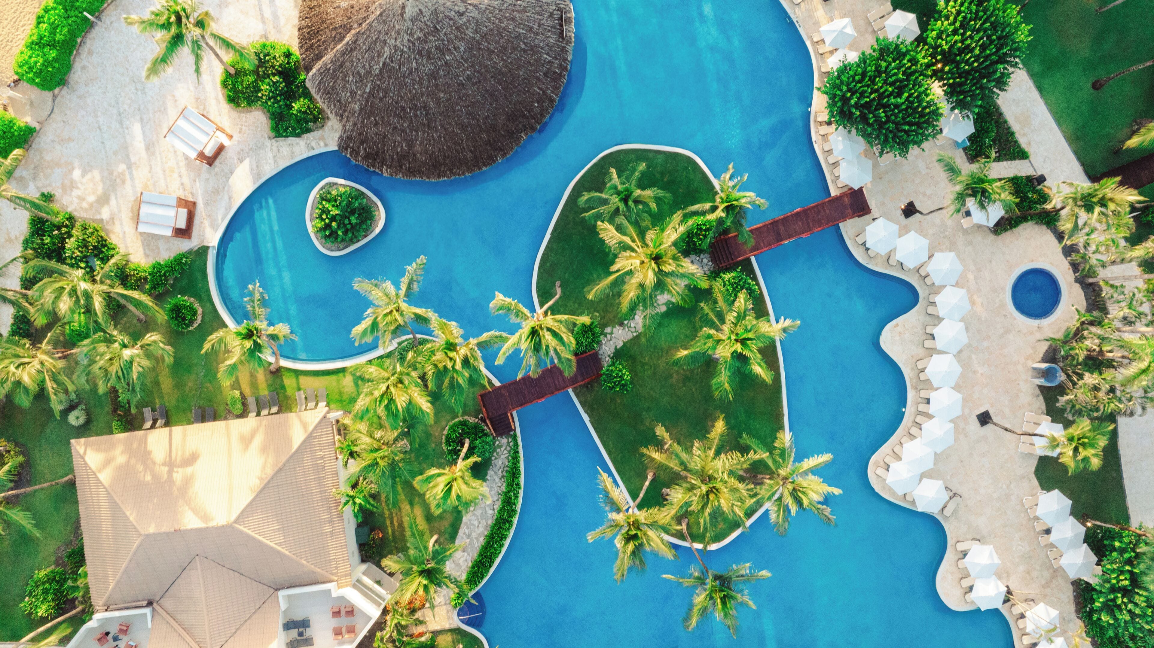 Luchtbeeld van een resort met een groot zwembad, palmbomen en loungegedeeltes.