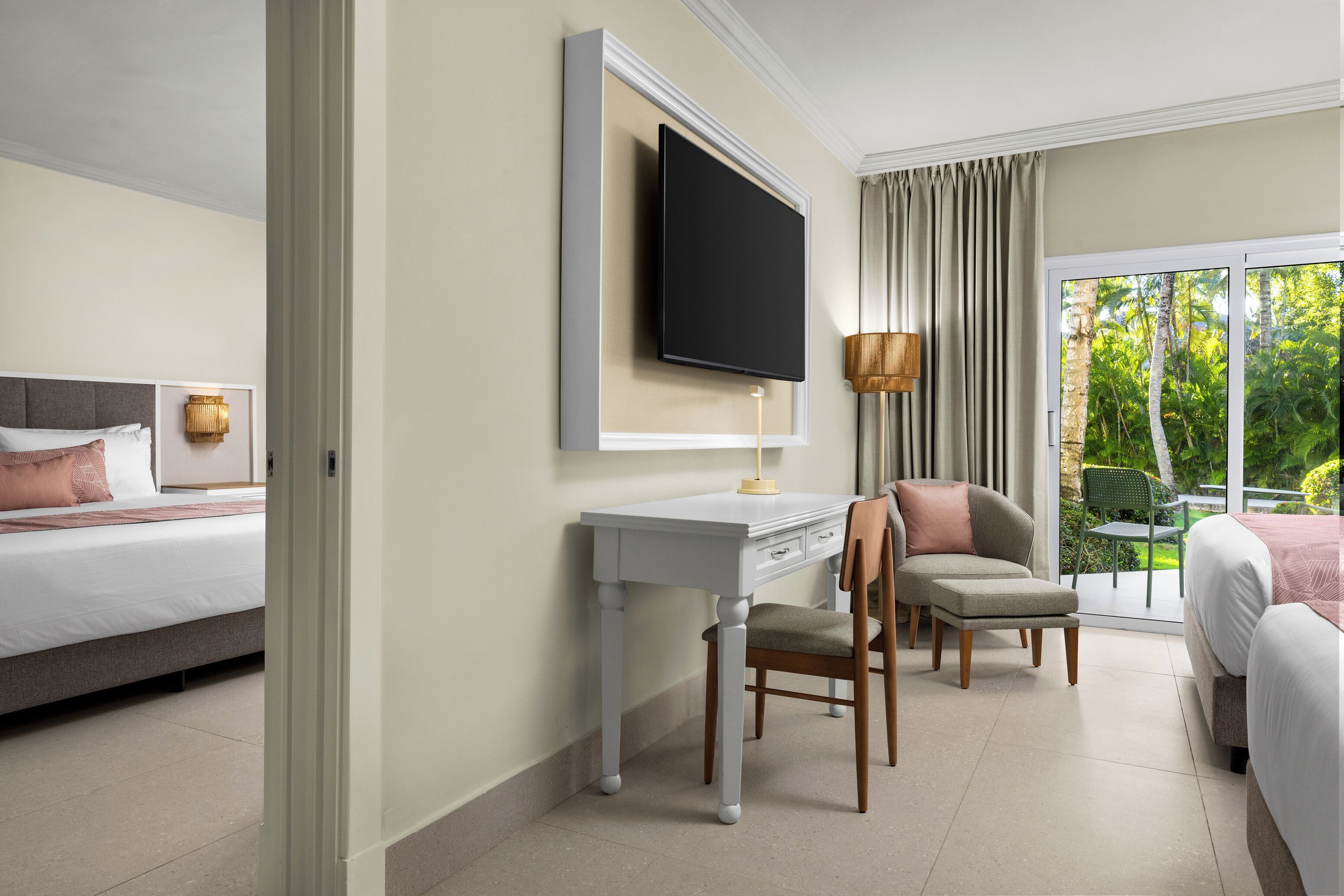 Une chambre d’hôtel avec un lit, un bureau, une chaise, une télévision et une vue sur la verdure par la fenêtre.