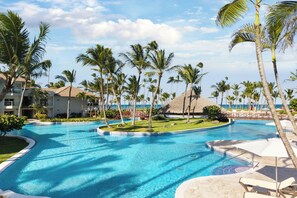 Ein Hotelpool mit Palmen, einer strohgedeckten Struktur und Blick auf den Ozean.