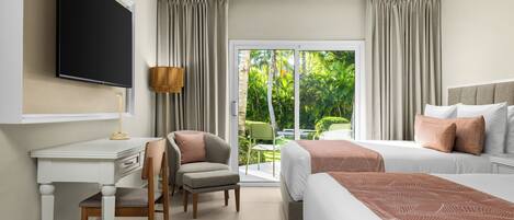 A hotel room with a flat-screen TV, a desk with a chair, two beds with pillows, a lamp, and a sliding glass door to a garden.
