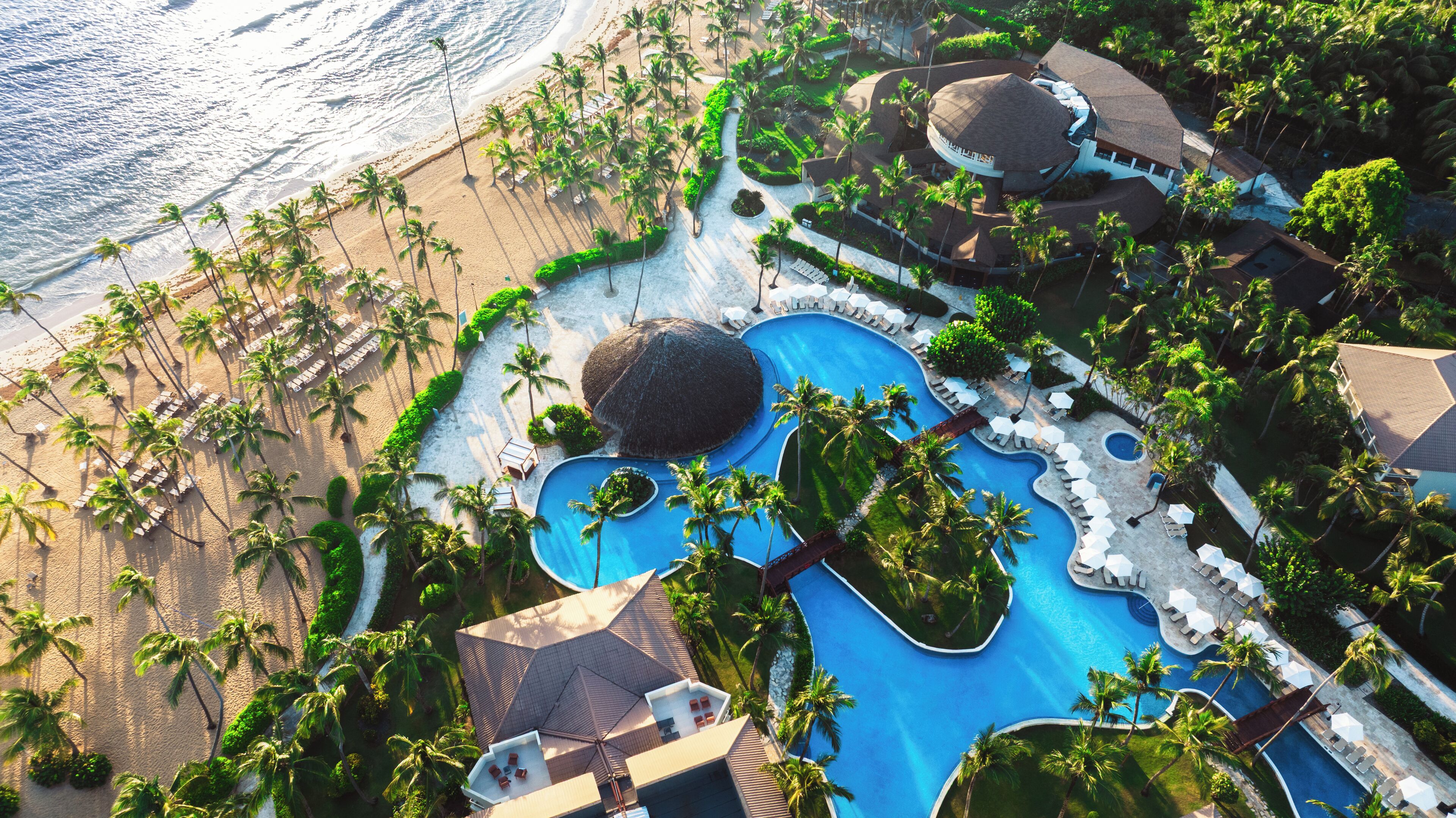 Luchtbeeld van een resort met een groot zwembad, strand en palmbomen.