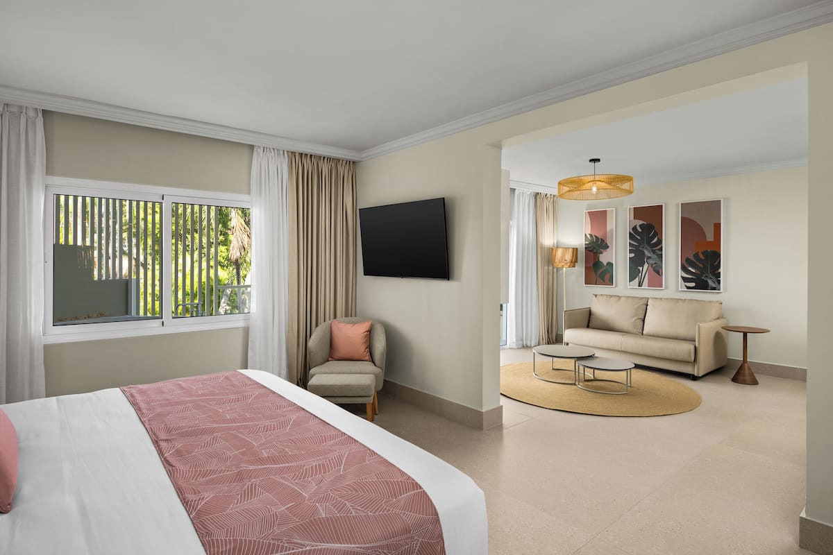 A hotel room with a bed, a sofa, a TV, and artwork on the wall.