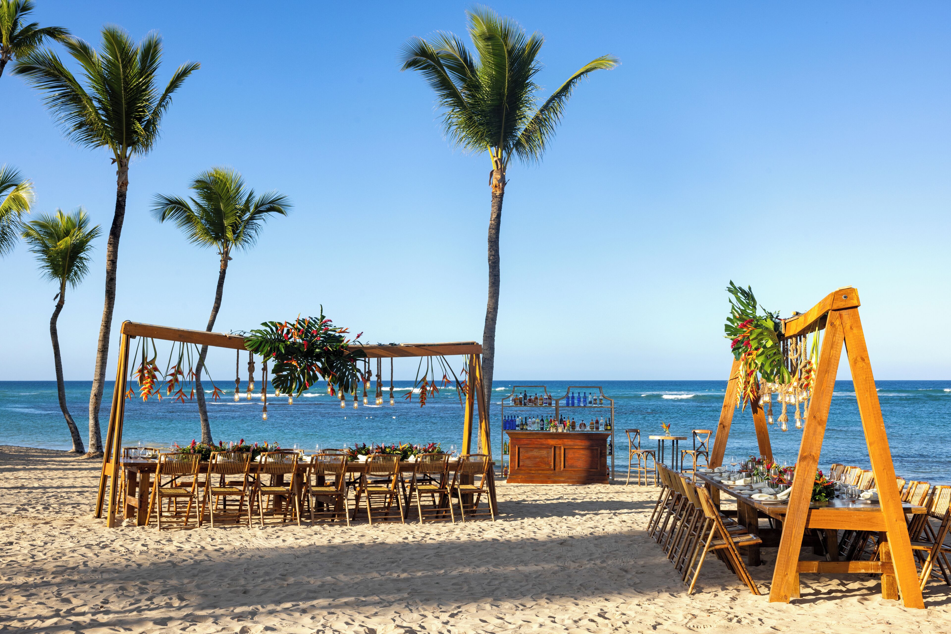 Une cérémonie de mariage organisée sur la plage, avec une arche en bois, des tables, des chaises et un bar.
