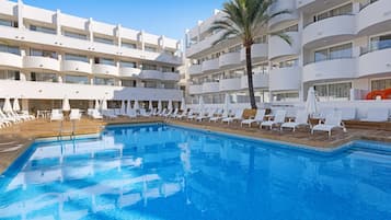 Un hotel con piscina, sillas de descanso y una palmera.