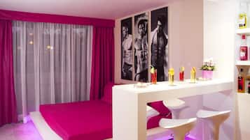 Un dormitorio moderno con una cama rosa, un escritorio blanco con taburetes altos y un ventanal con cortinas traslúcidas.