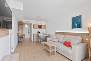 A modern living room with a sofa, a coffee table, and a dining area with chairs and a kitchen in the background. - Palmanova Beach Apartments by TRH (Calvia)