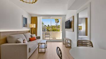 Habitación de hotel moderna con sofá, una mesita, una silla, televisor y balcón con vistas a la ciudad.