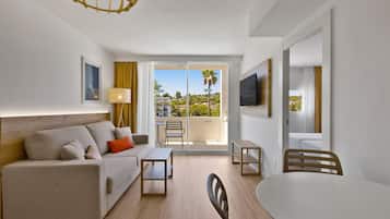 Habitación de hotel moderna con sofá, una mesita, una silla, televisor y balcón con vistas a la ciudad.