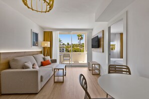 Ein modernes Hotelzimmer mit einer Couch, einem kleinen Tisch, einem Sessel, einem Fernseher und einem Balkon mit Blick auf die Stadt.