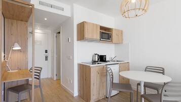Cocina compacta con armarios de madera, microondas, hervidor y un comedor con sillas y mesa.