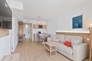 A modern living room with a sofa, a coffee table, and a dining area with chairs and a kitchen in the background. - Palmanova Beach Apartments by TRH (Calvia)