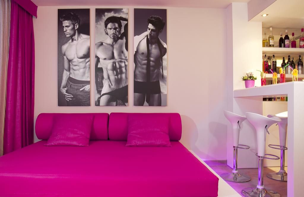 Una habitación de hotel con una cama, una zona de bar con taburetes y una pared con tres cuadros enmarcados.