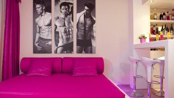 Una habitación de hotel con una cama, una zona de bar con taburetes y una pared con tres cuadros enmarcados.
