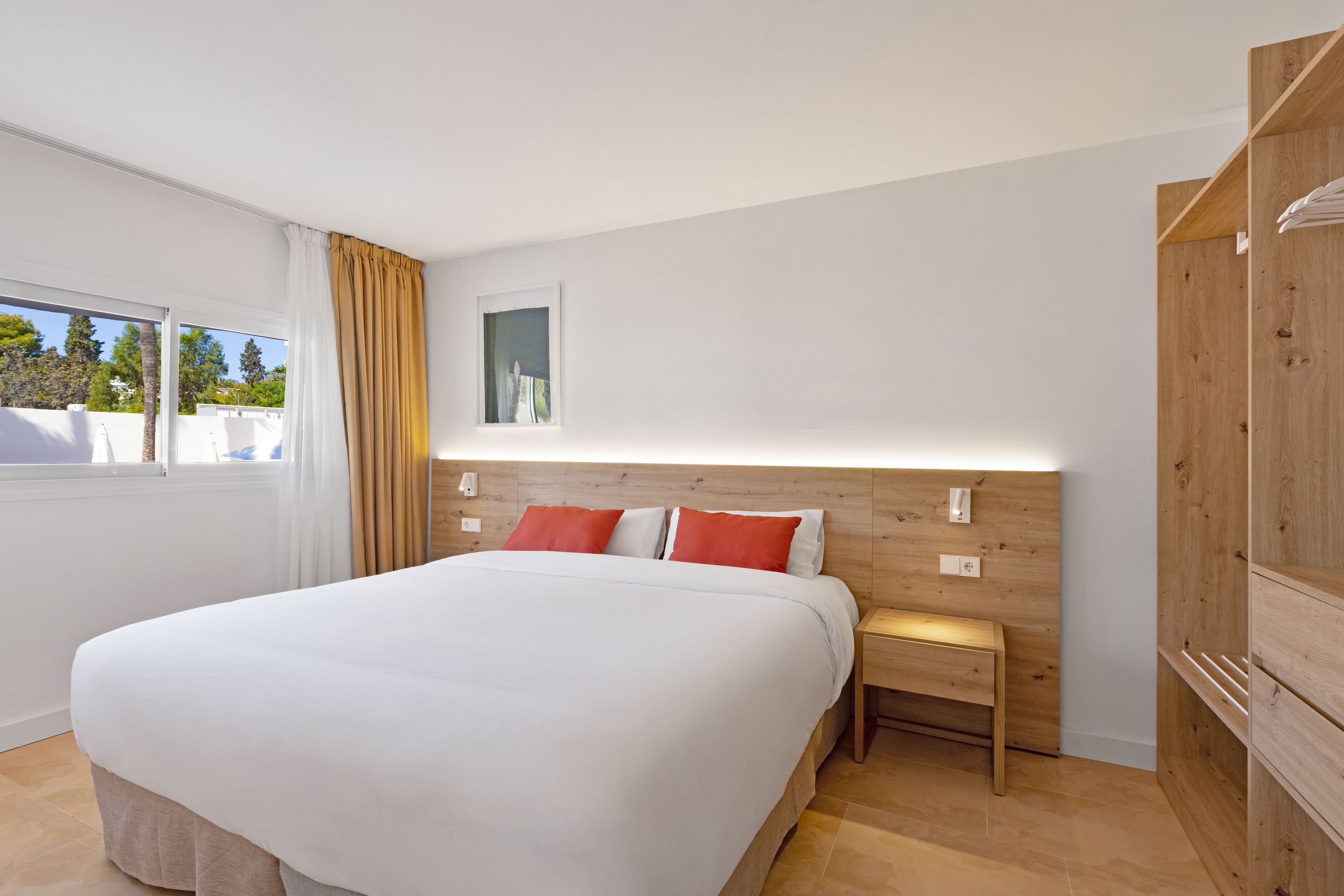 Un dormitorio moderno con una cama grande, cabecera de madera, mesita de noche y vistas al exterior.