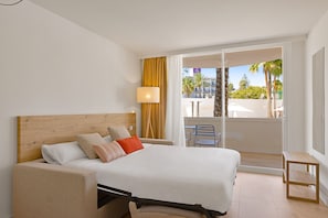 Habitación de hotel con cama, mesita de noche, lámpara y vistas al exterior.
