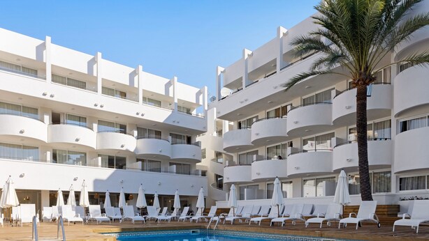 A swimming pool with lounge chairs and umbrellas, surrounded by multi-story buildings with balconies. - Palmanova Beach Apartments by TRH (Calvia)