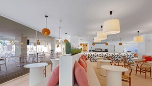 A modern cafe with white furniture, round tables, and hanging pendant lights. - Palmanova Beach Apartments by TRH (Calvia)