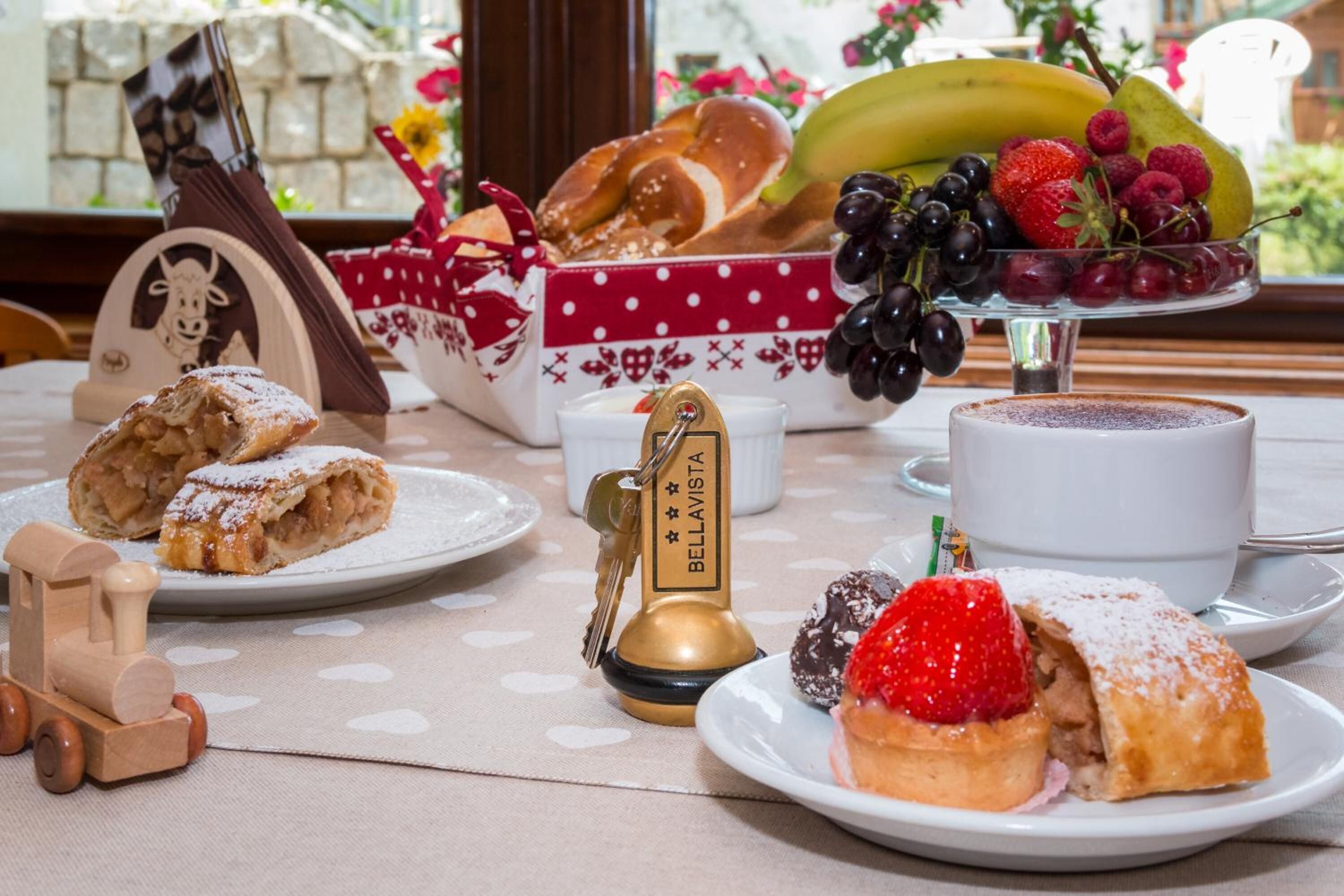 Una mesa con pasteles, un tren de juguete de madera, una campana y una exhibición de frutas.