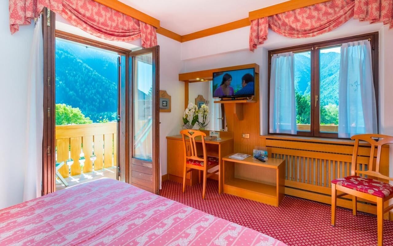 A hotel room with a bed, a desk, a chair, a television, and a balcony with a mountain view.