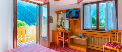 A hotel room with a bed, a desk, a chair, a television, and a balcony with a mountain view.