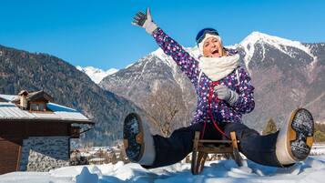 Eine Person sitzt auf einem hölzernen Stuhl in verschneiter Landschaft, mit Bergen im Hintergrund.