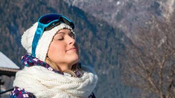 Una persona con gorro y bufanda, de pie al aire libre con montañas al fondo.