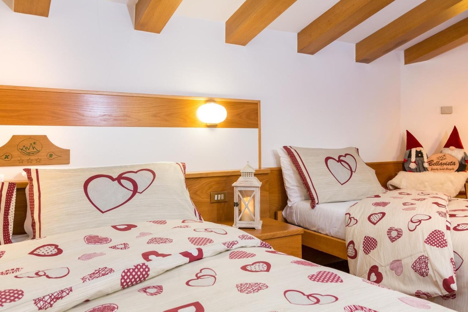 A hotel room with two beds, each with heart-patterned bedding, wooden headboards, and a night light.