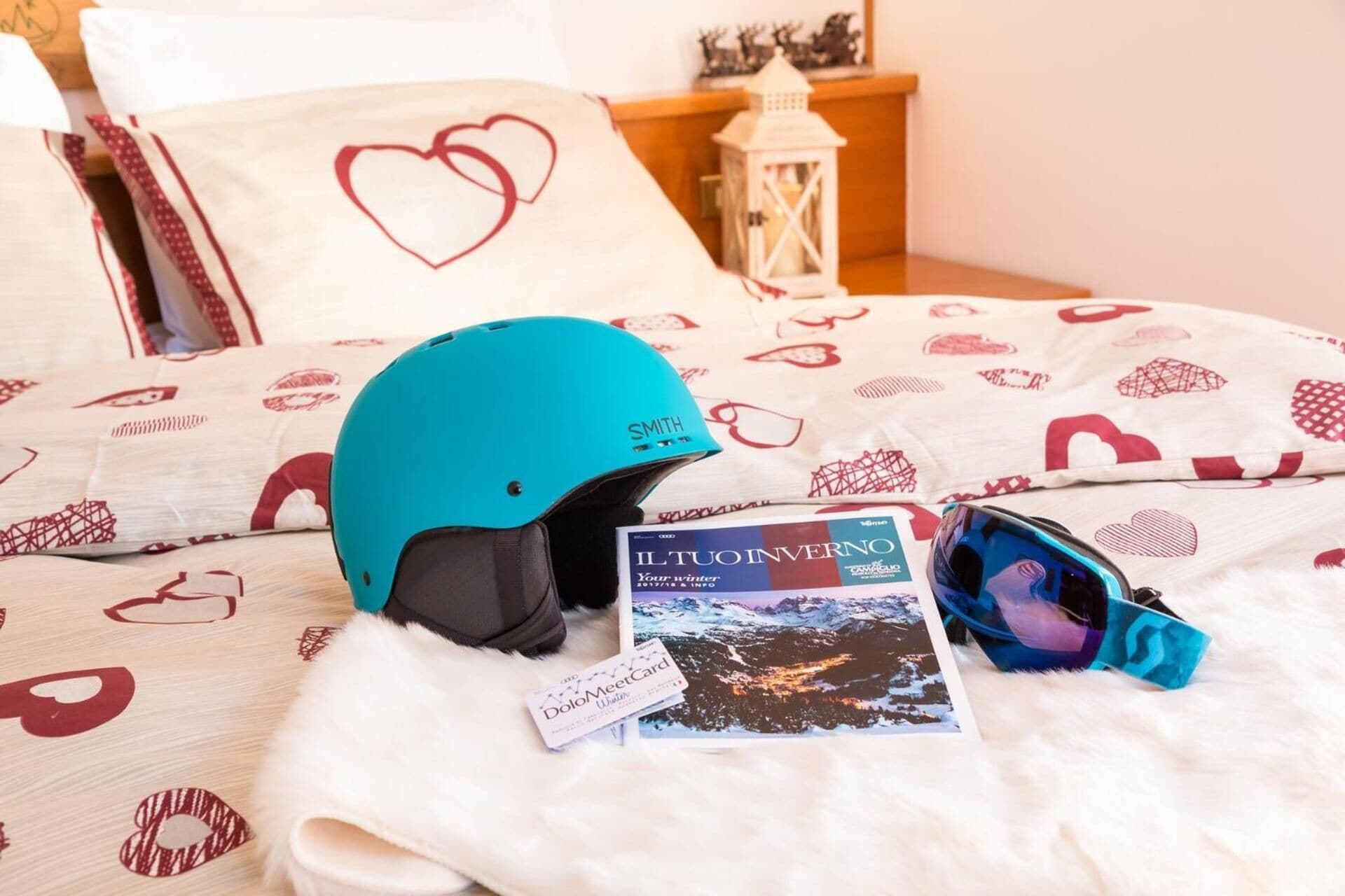Een bed met een blauwgroene helm, een zonnebril, een tijdschrift en een badge op een zachte witte deken.