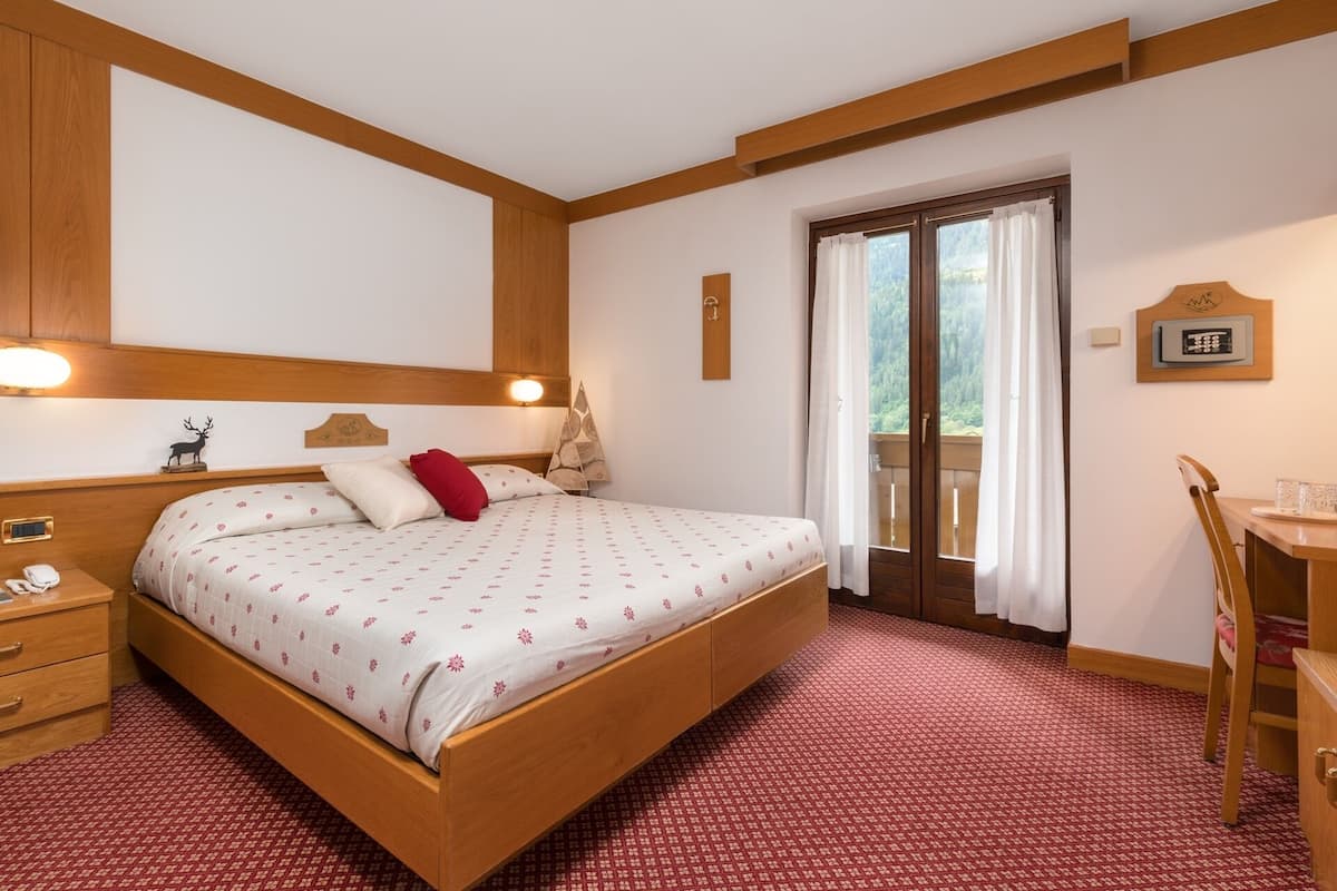 Ein Hotelzimmer mit einem hölzernen Bett, einem Schreibtisch und Blick ins Freie durch eine Tür.