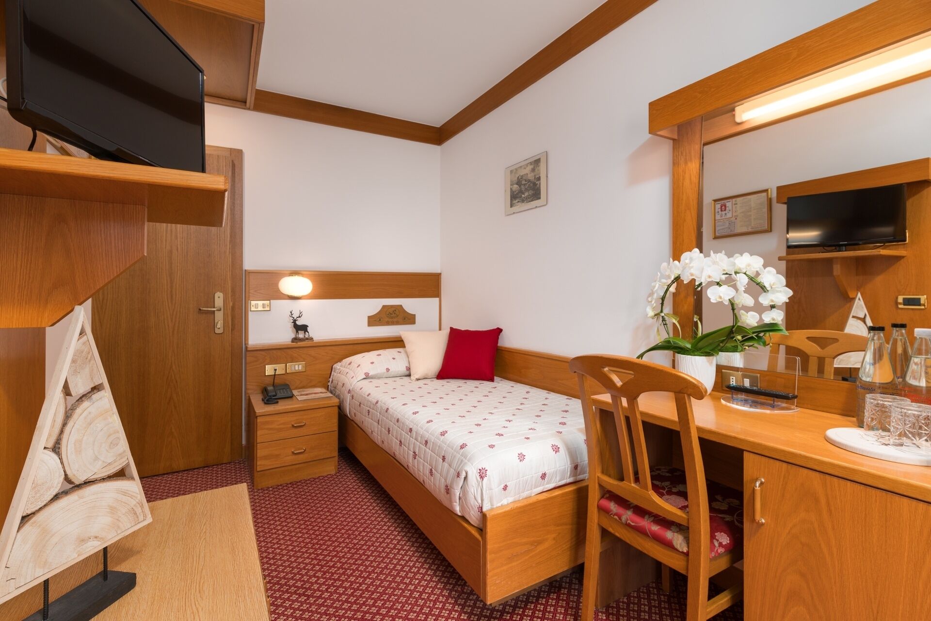 Habitación de hotel pequeña con cama, mesita de noche, lámpara y escritorio con silla.