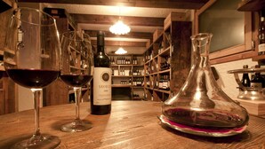 A wooden bar with wine glasses and bottles, shelves with wine bottles, and a wine bottle labeled "SASSICA 2006". - Hotel Gianna (Tre Ville)
