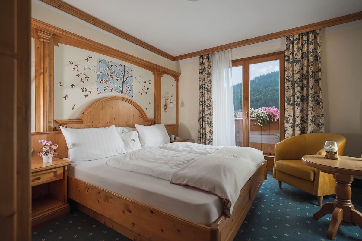 A hotel room with a wooden bed, a small table with a glass, a chair, and a window with curtains.