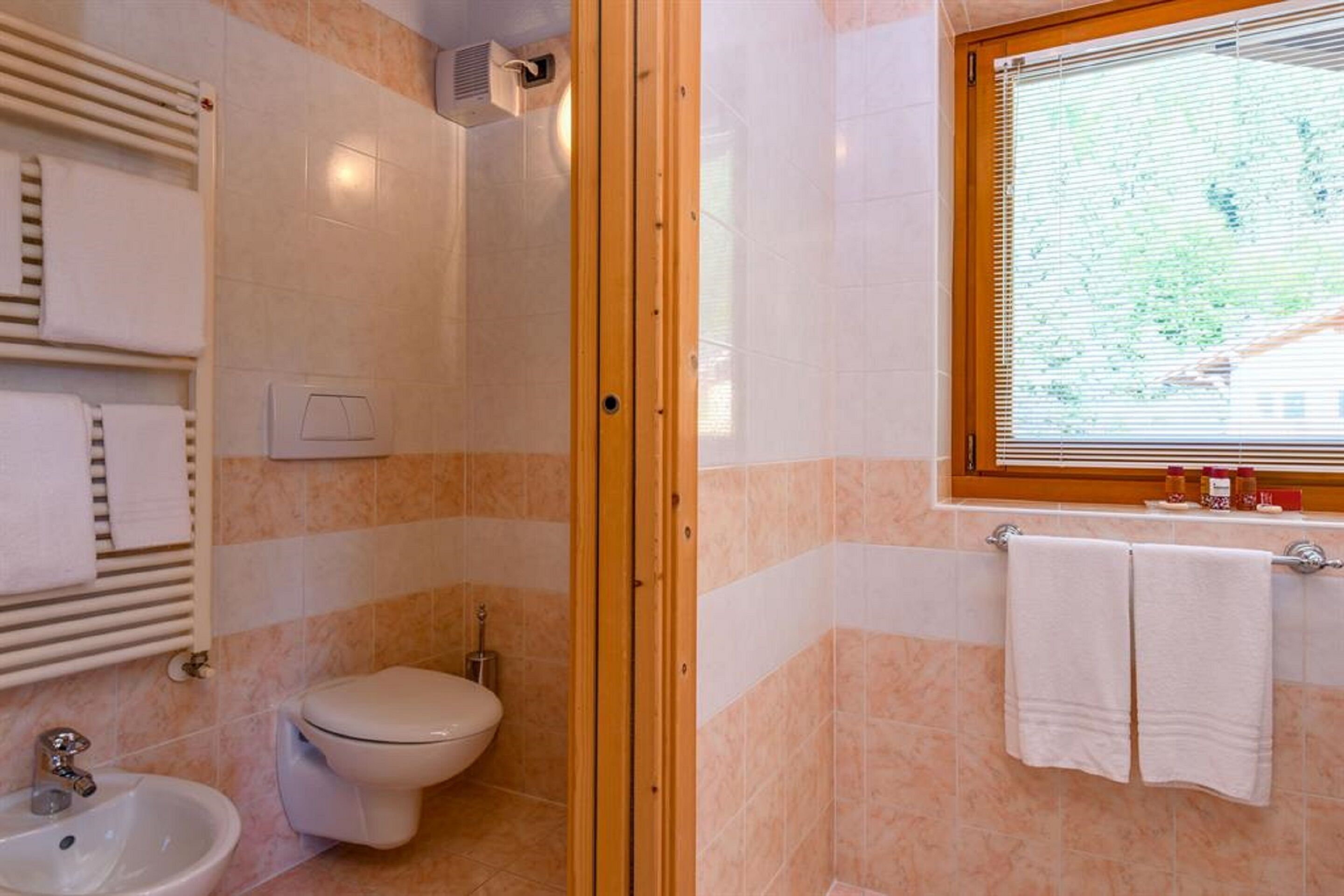 Un baño con ducha, inodoro, lavabo y ventana con persianas.