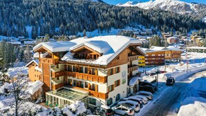 A multi-story hotel with a snow-covered roof, a glass entrance, and a parking area with several cars. - Hotel Gianna (Tre Ville)