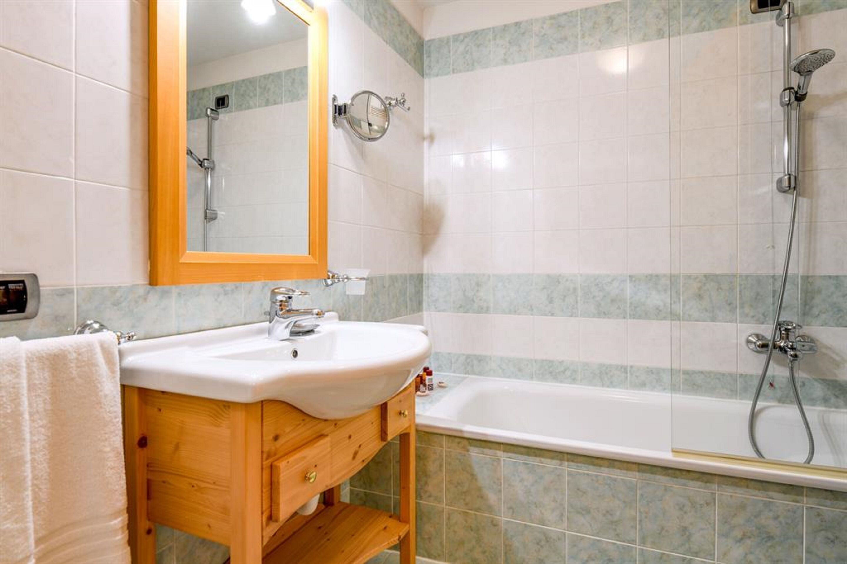 Un baño con tocador de madera, lavabo blanco, espejo y zona de ducha.