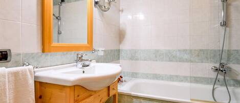 Un baño con tocador de madera, lavabo blanco, espejo y zona de ducha.