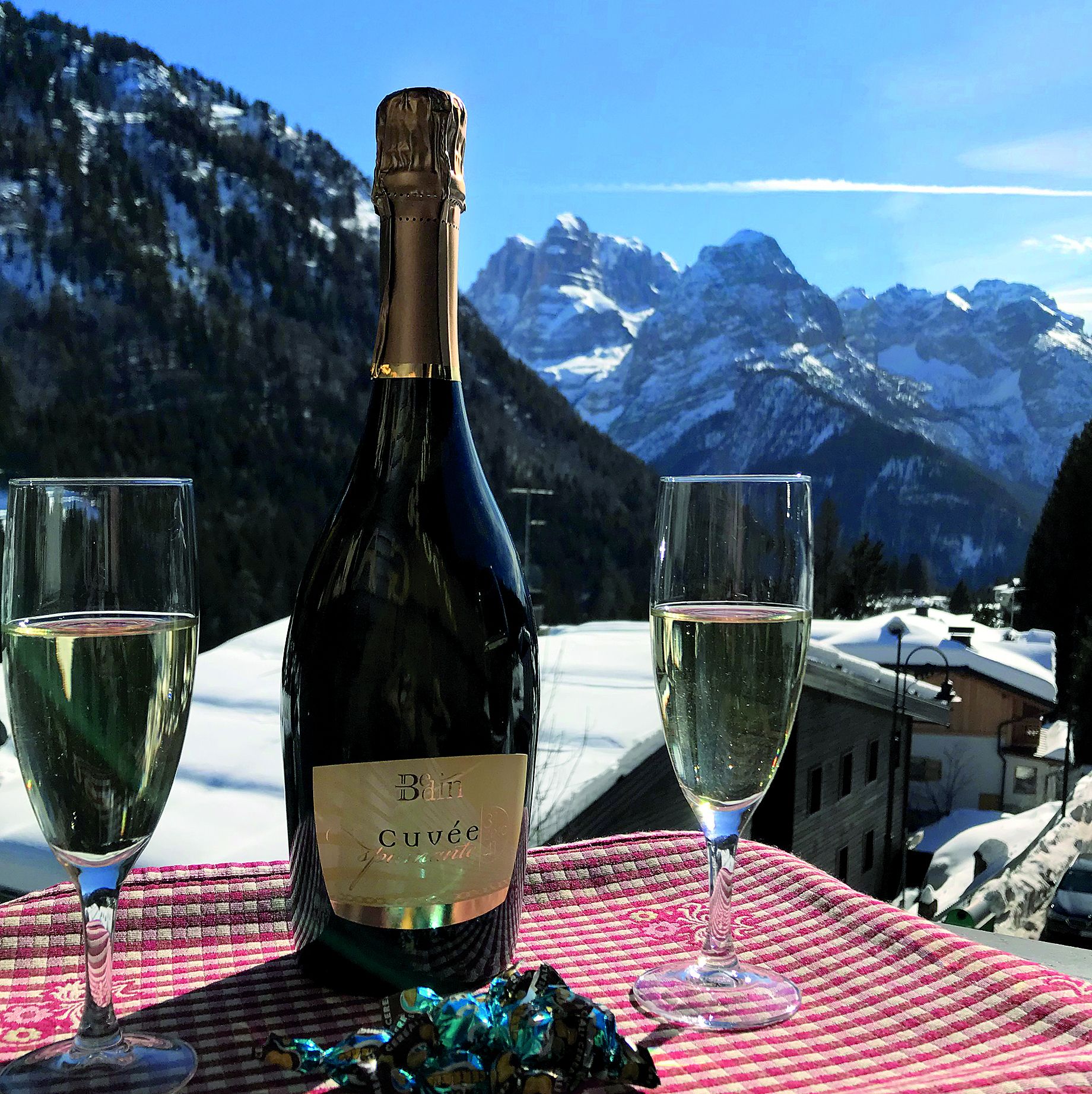 A bottle of wine and two glasses on a table with a mountain view in the background.