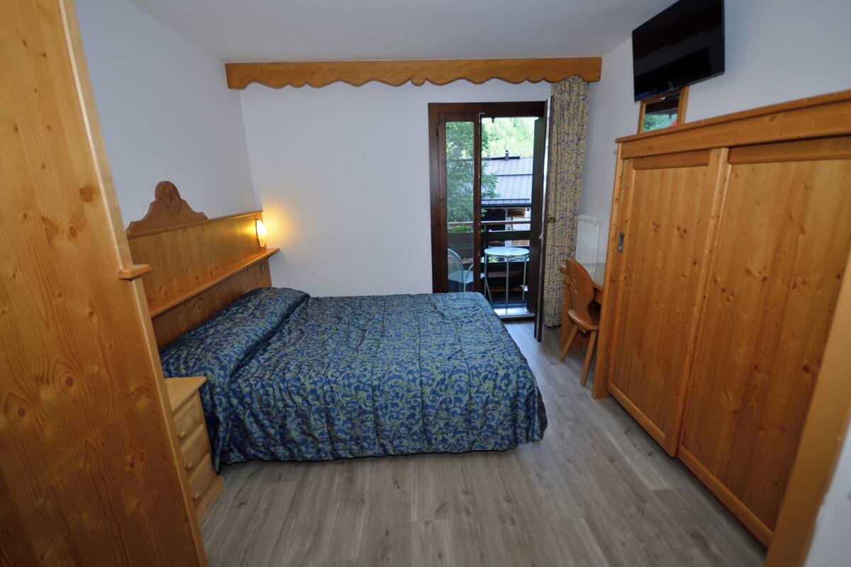 Un dormitorio con una cama, armario de madera y televisor en la pared.